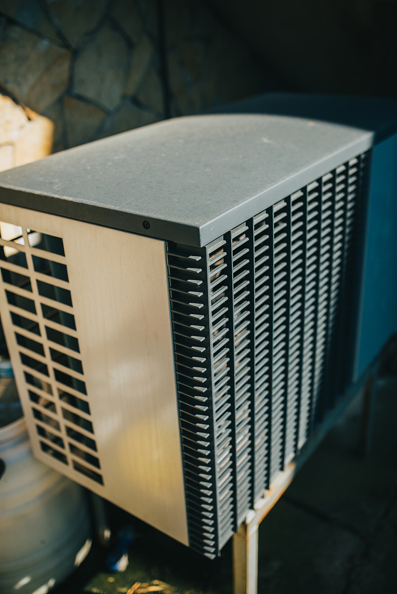 Buitenunit van een warmtepomp tegen de gevel in een tuin